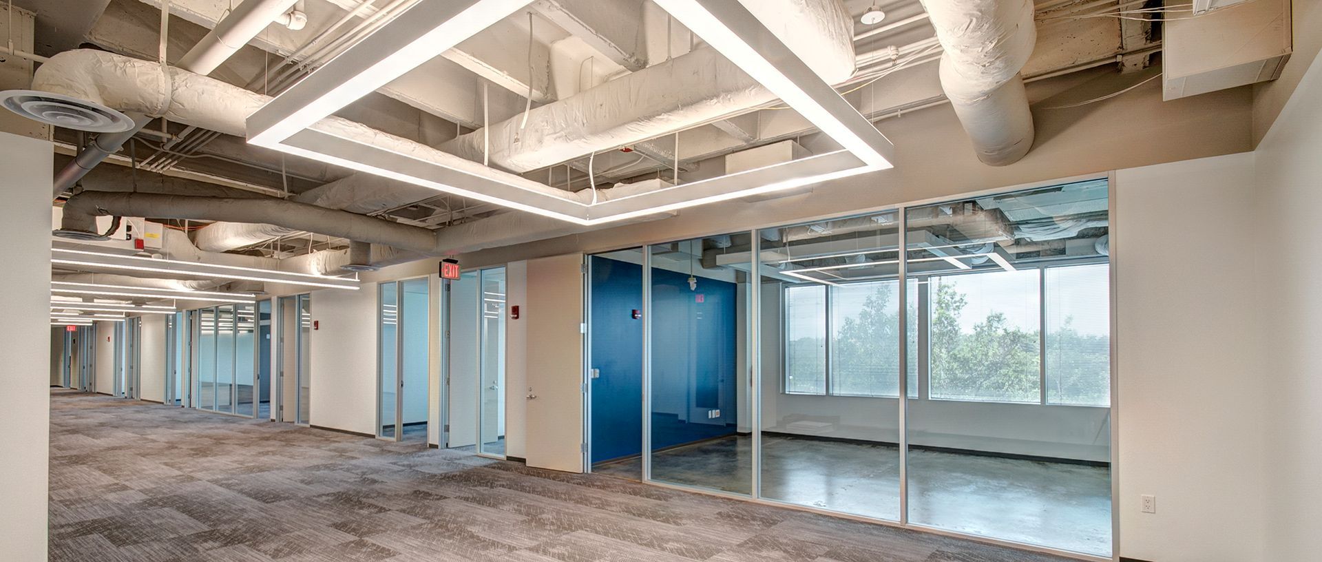 Empty modern office interior with glass-walled rooms, white ceiling beams, and carpeted floor