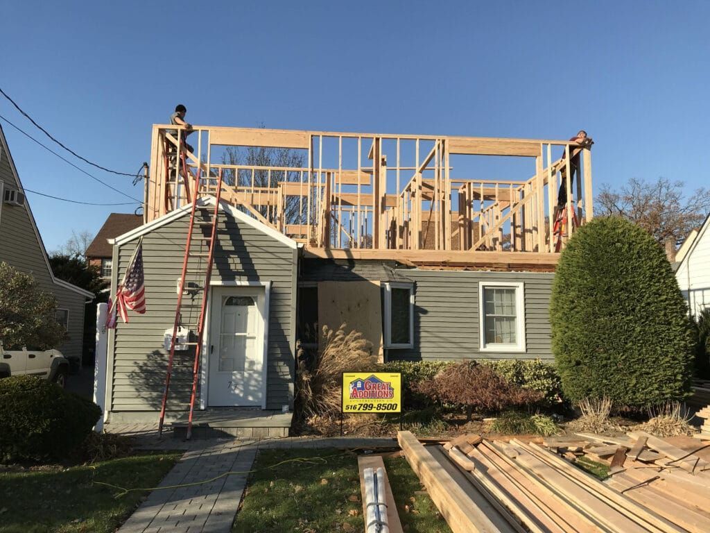 Concrete foundation under construction beside a red brick house with blue safety fencing and dirt piles