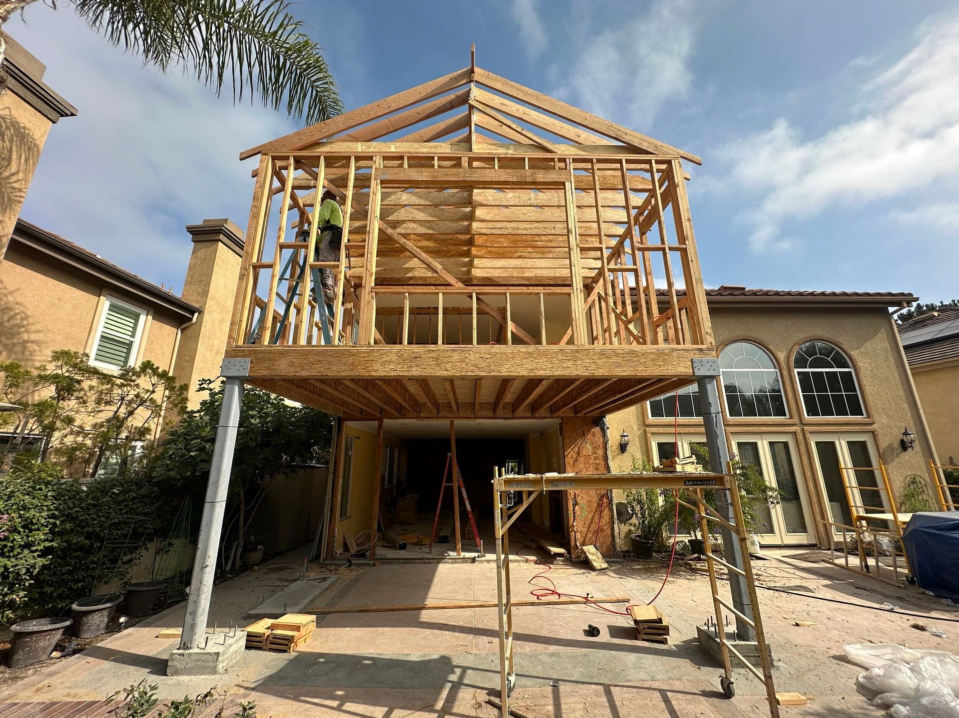 House under construction with wooden framing and scaffolding in front of a large home.