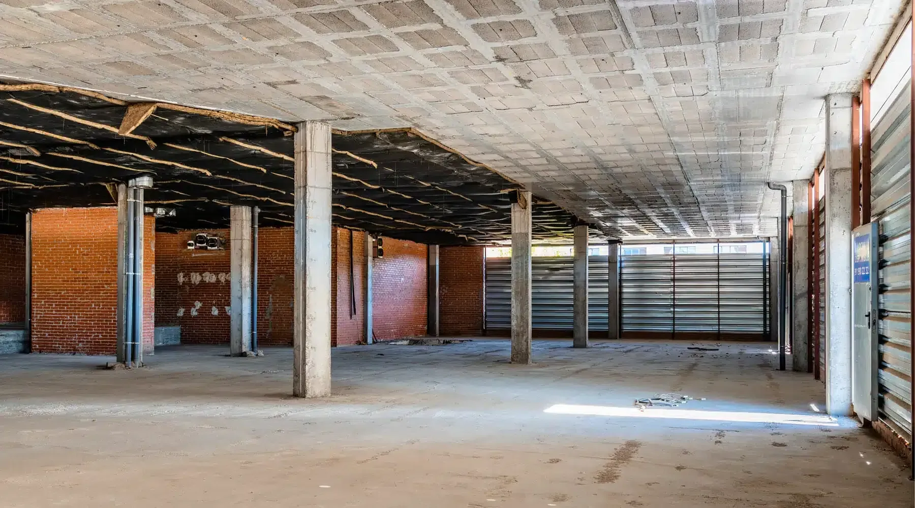 Empty unfinished industrial interior with concrete pillars, exposed ceiling, and large windows