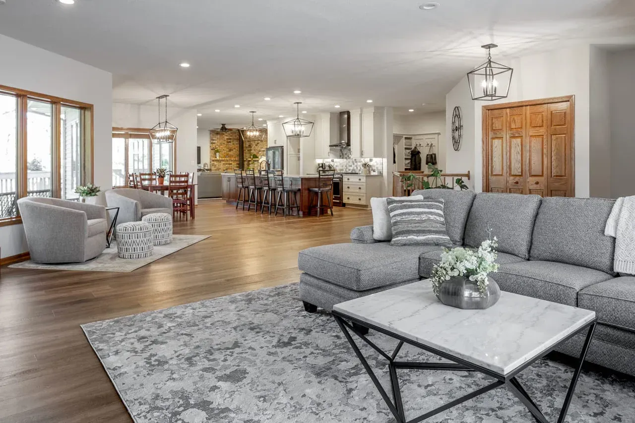 Spacious open-concept living room with gray sofas, wood floors, and a dining area in the background