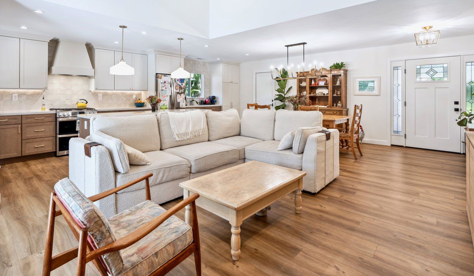 Bright open-plan living room with beige sectional, wood coffee table, dining area, and kitchen in the background
