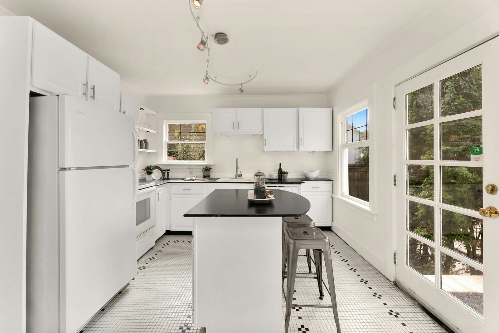 Bright white kitchen with island, bar stool, large windows, and garden-view French doors.
