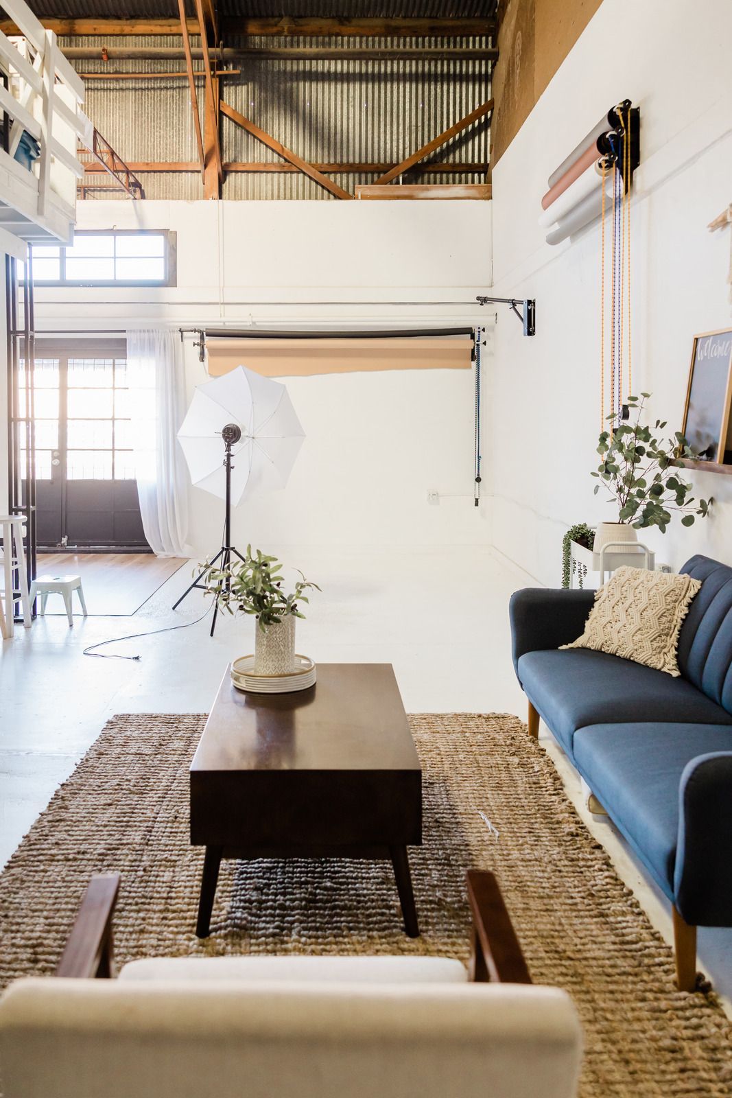 Bright loft living room with blue sofa, coffee table, rug, and plants beneath high industrial windows