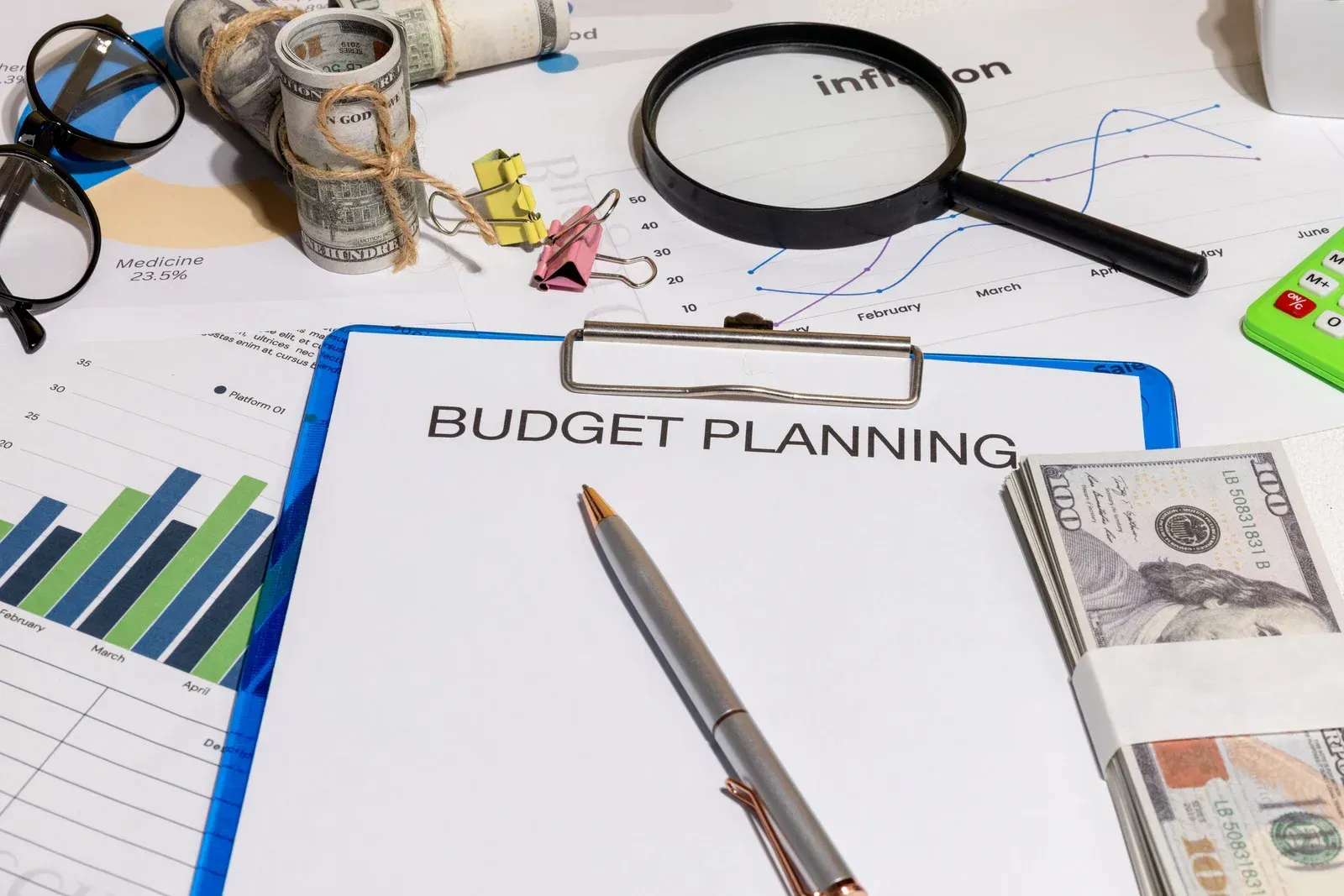 Budget planning desk with charts, calculator, magnifying glass, and cash on papers