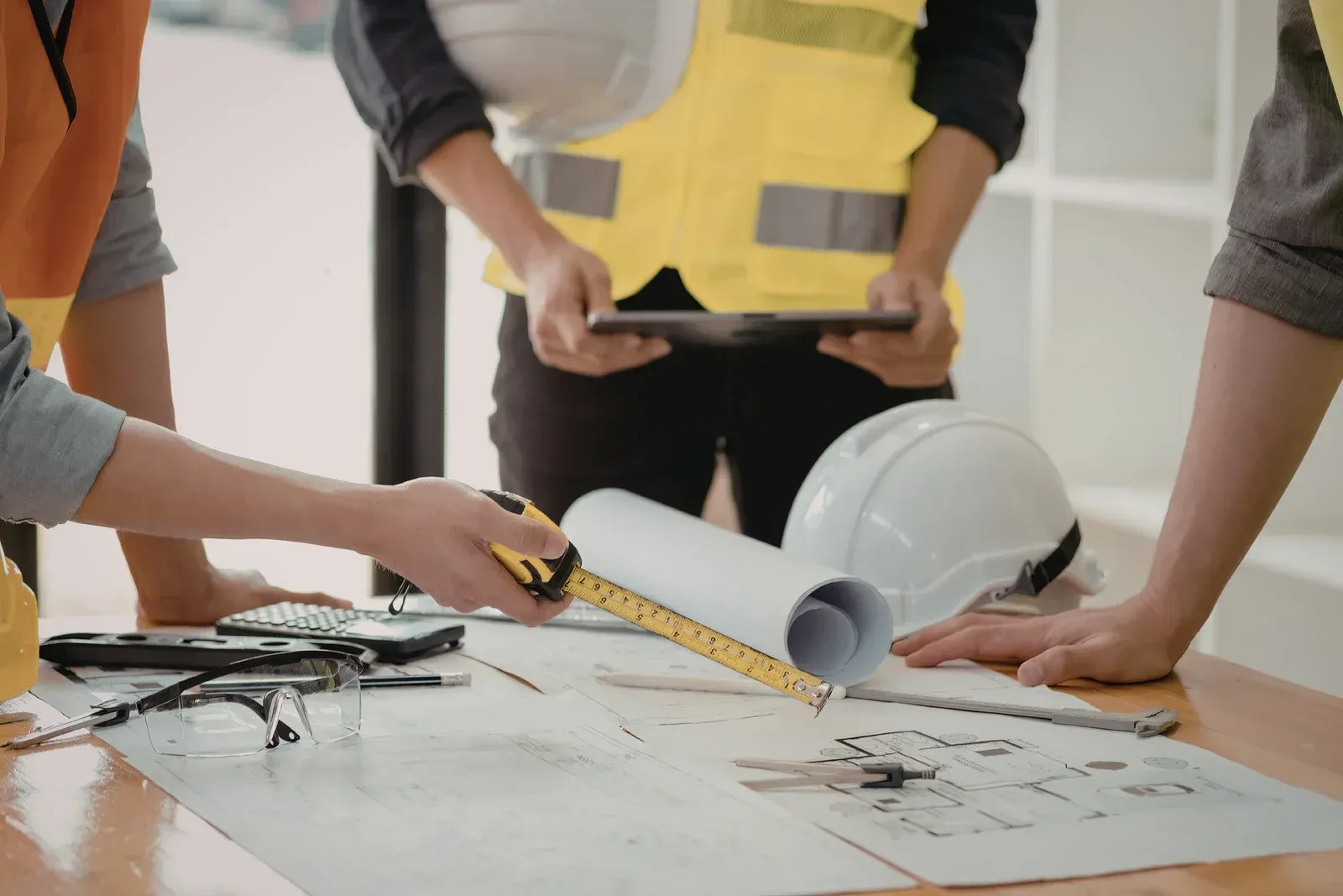 Construction workers reviewing plans with a hard hat and measuring tape on a table
