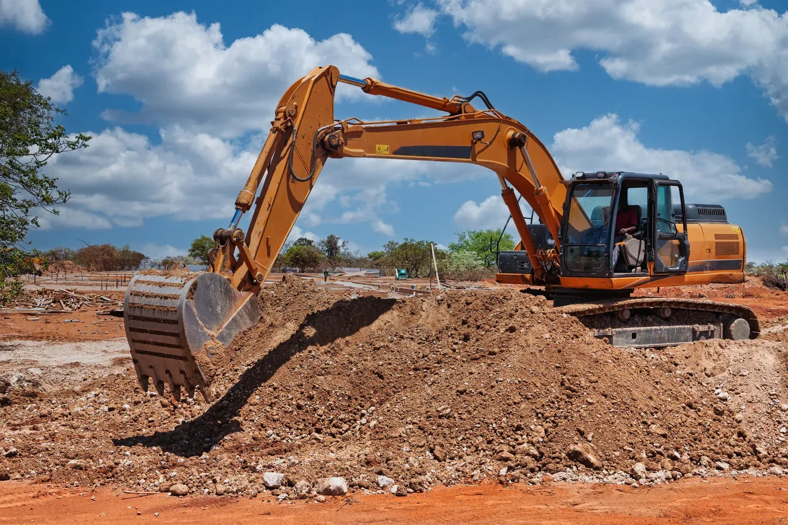Orange excavator digging a dirt mound at a construction site under a blue sky