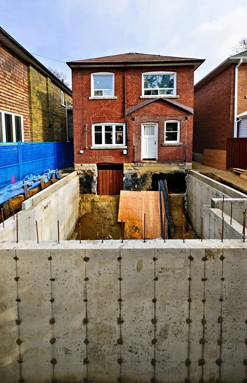 Partially built brick house with foundation work and construction materials in a narrow backyard