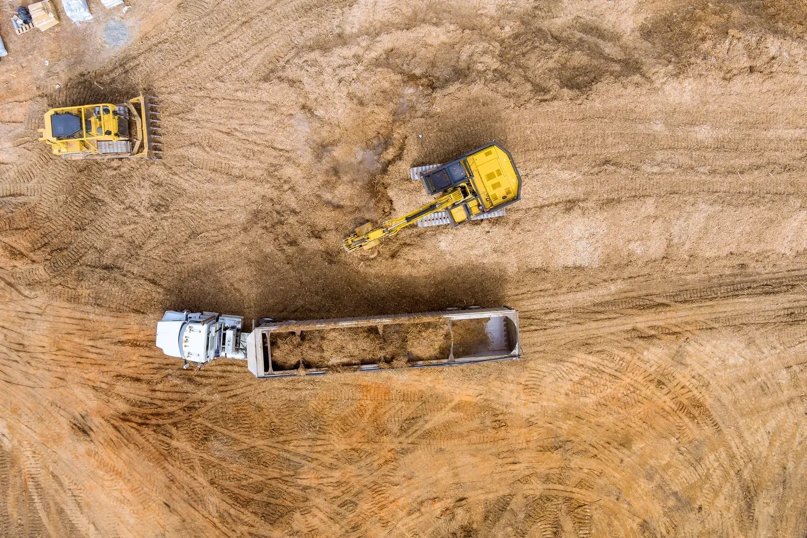 Aerial view of construction site with excavators, dump truck, and a white truck on dirt ground