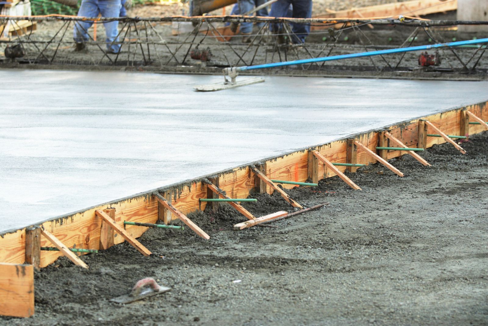 Concrete slab being poured on a construction site, with wooden forms and workers in the background