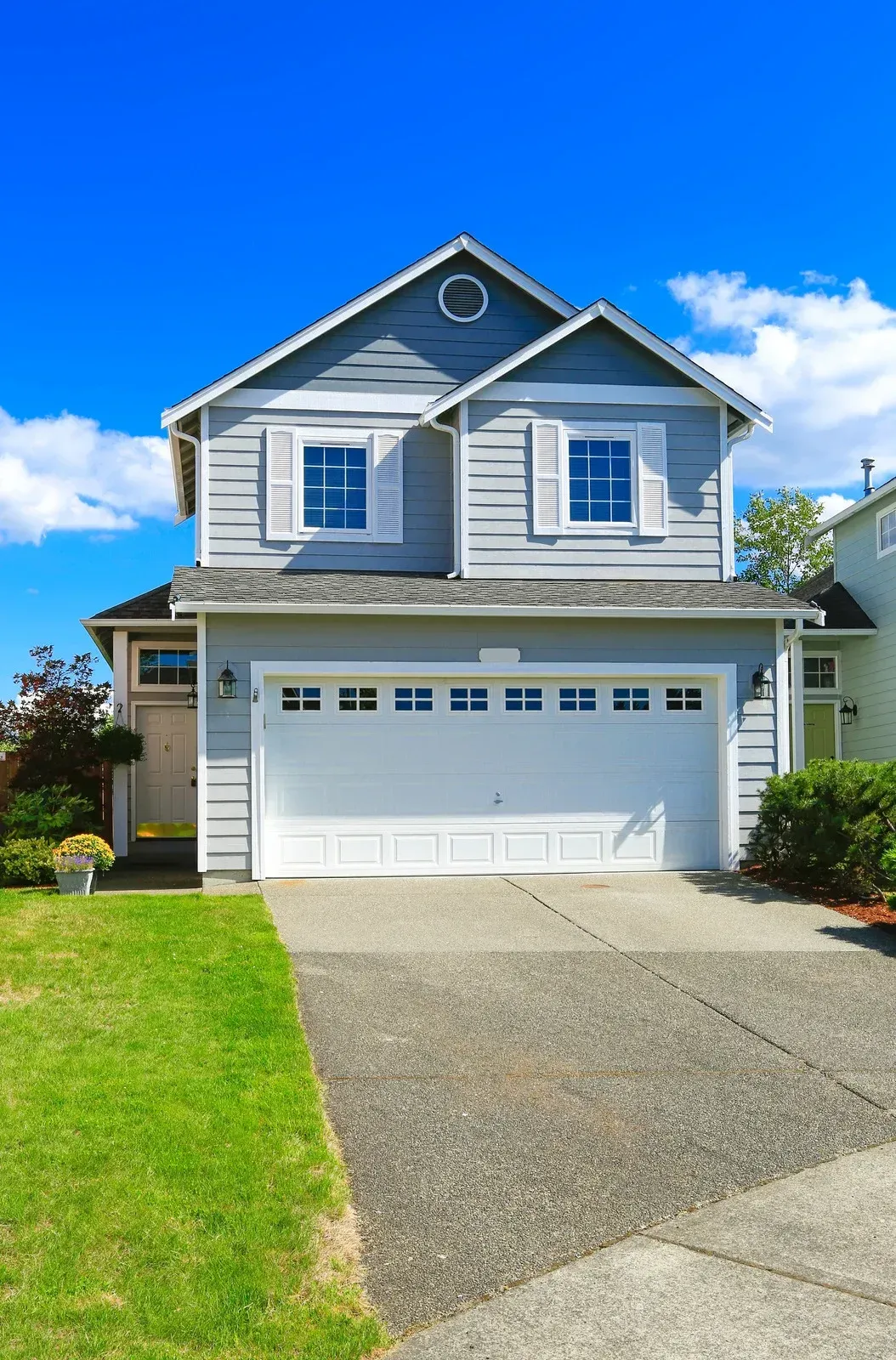 Two-story gray house with white trim and a two-car garage under a bright blue sky