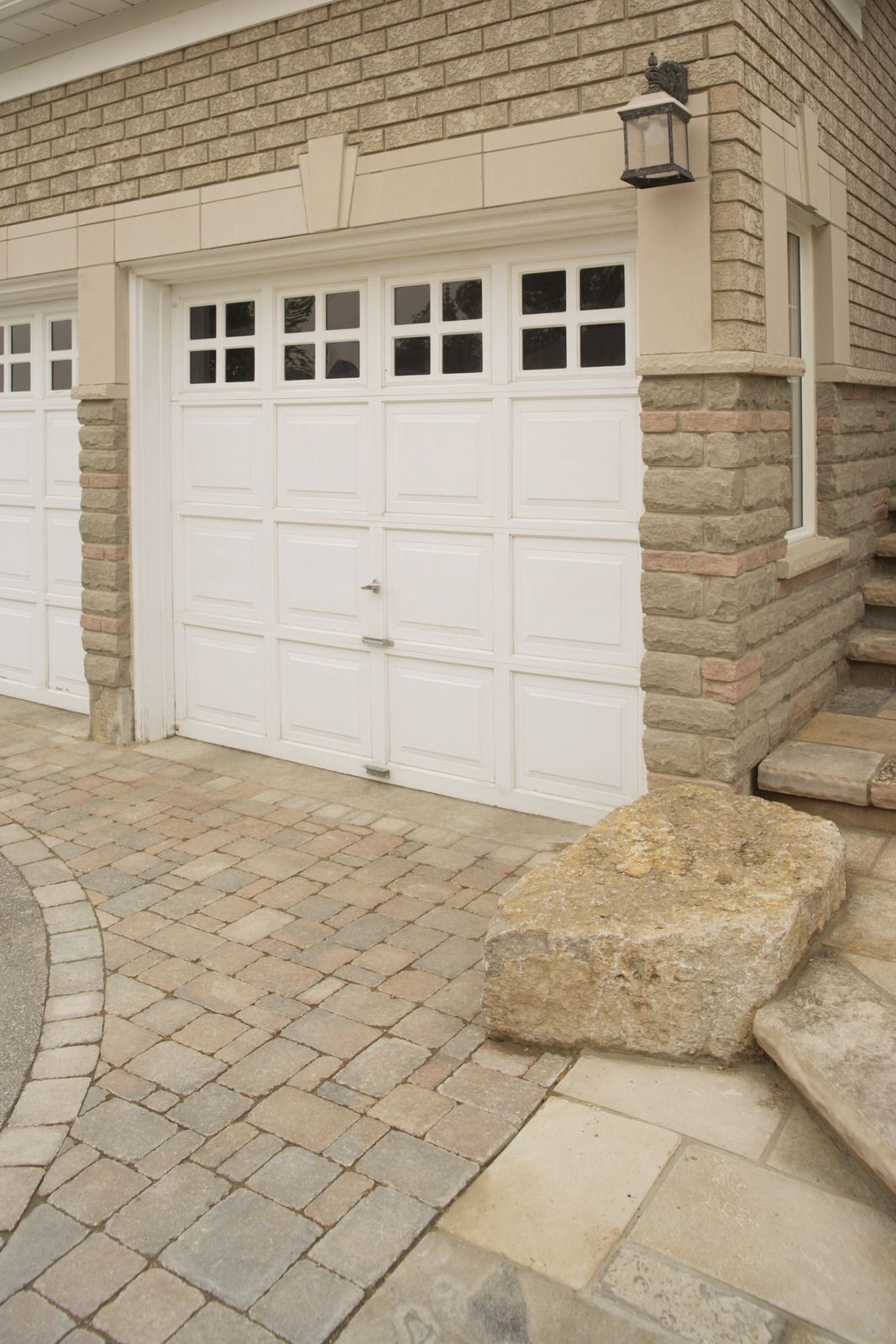White garage door beside stone steps and paved driveway at a beige brick house