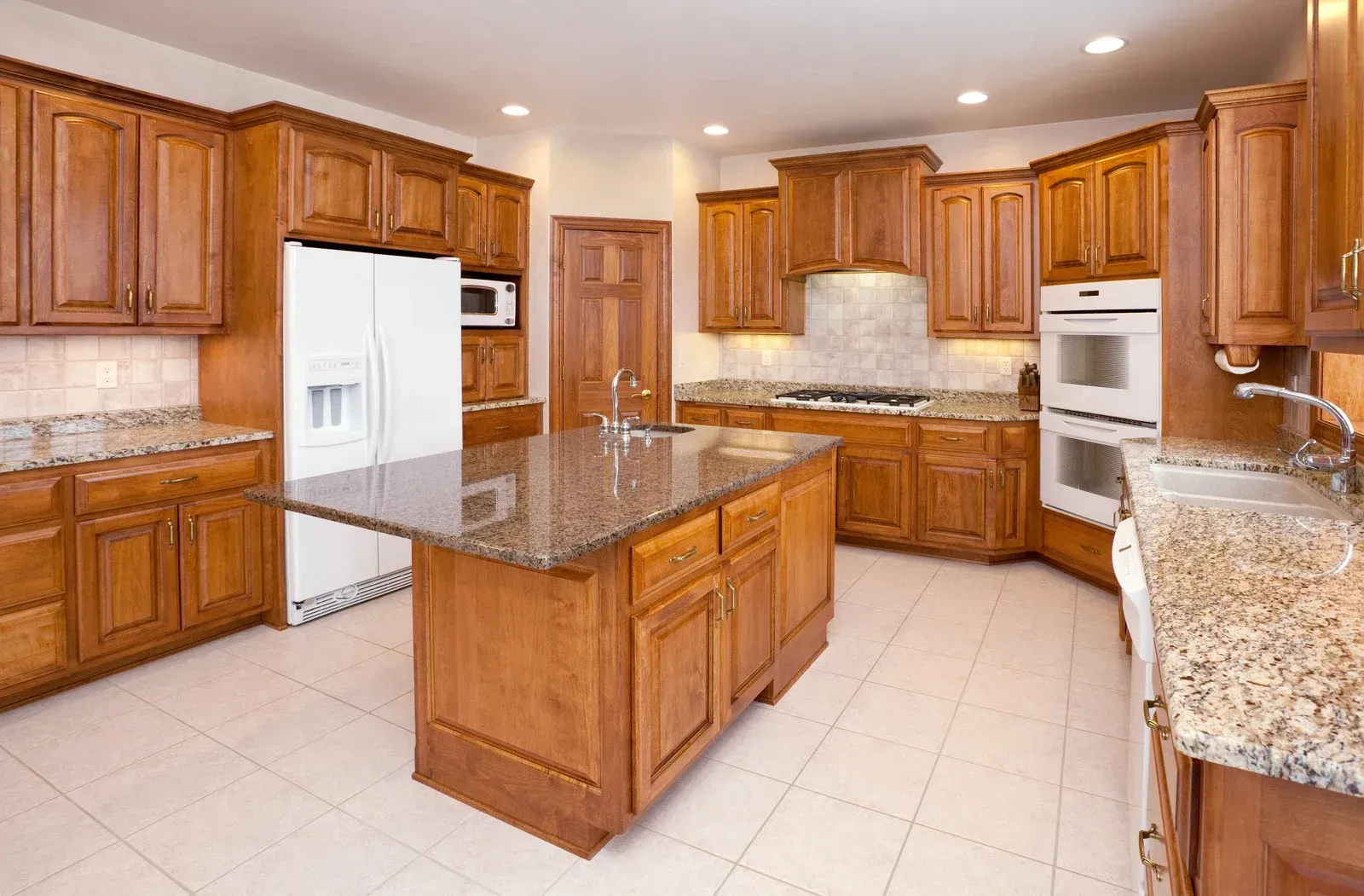 Spacious kitchen with wooden cabinets, granite countertops, island, white appliances, and tiled floor