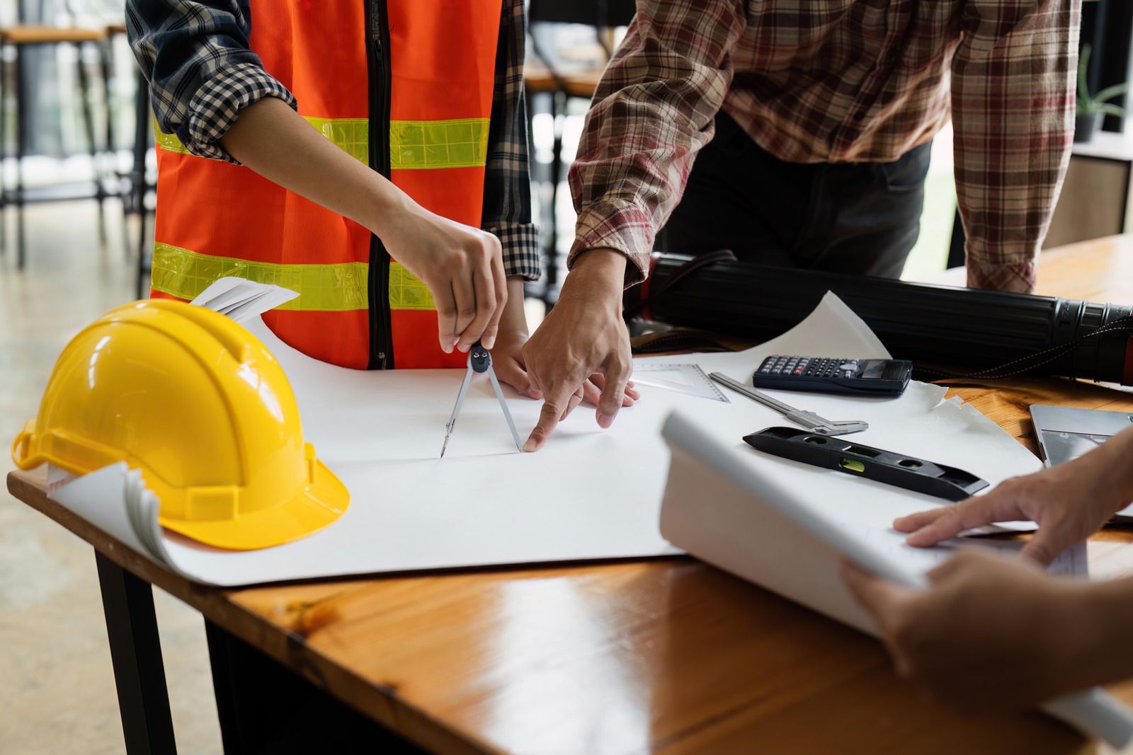 Engineers reviewing blueprints at a desk with a yellow hard hat and tools
