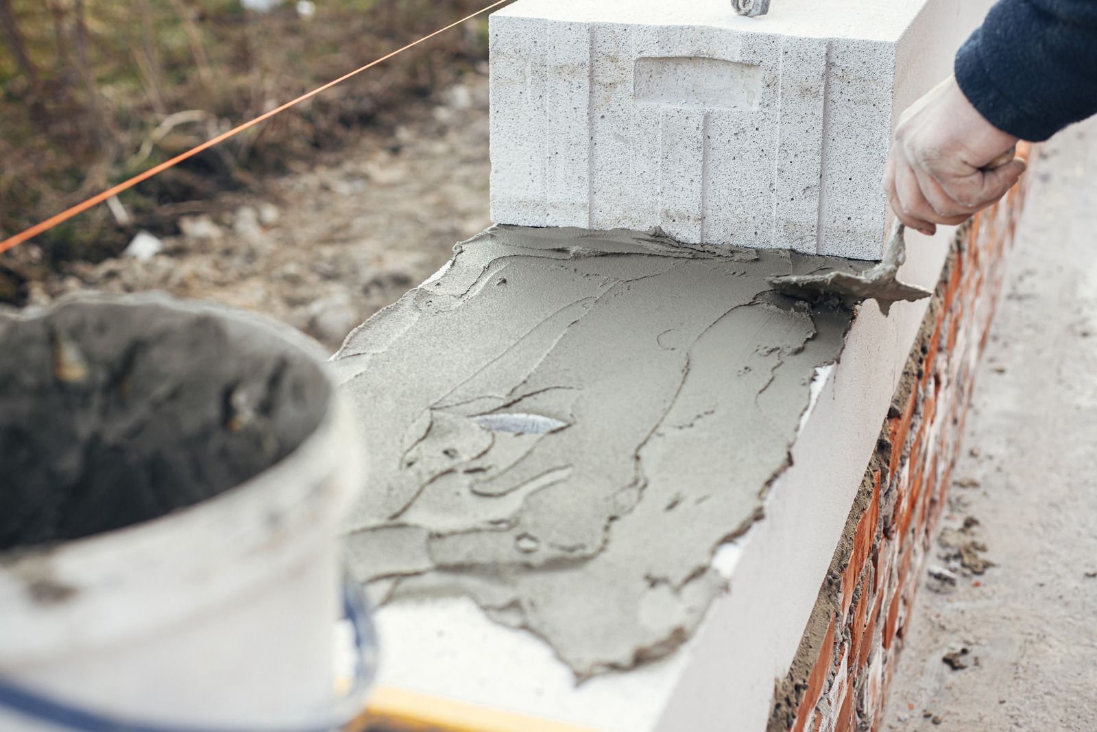 Concrete being spread on a brick wall cap by a worker's hand, with a bucket in the foreground