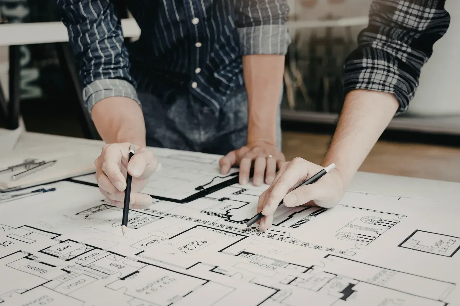 Hands working on architectural blueprints with pens and rulers on a drafting table