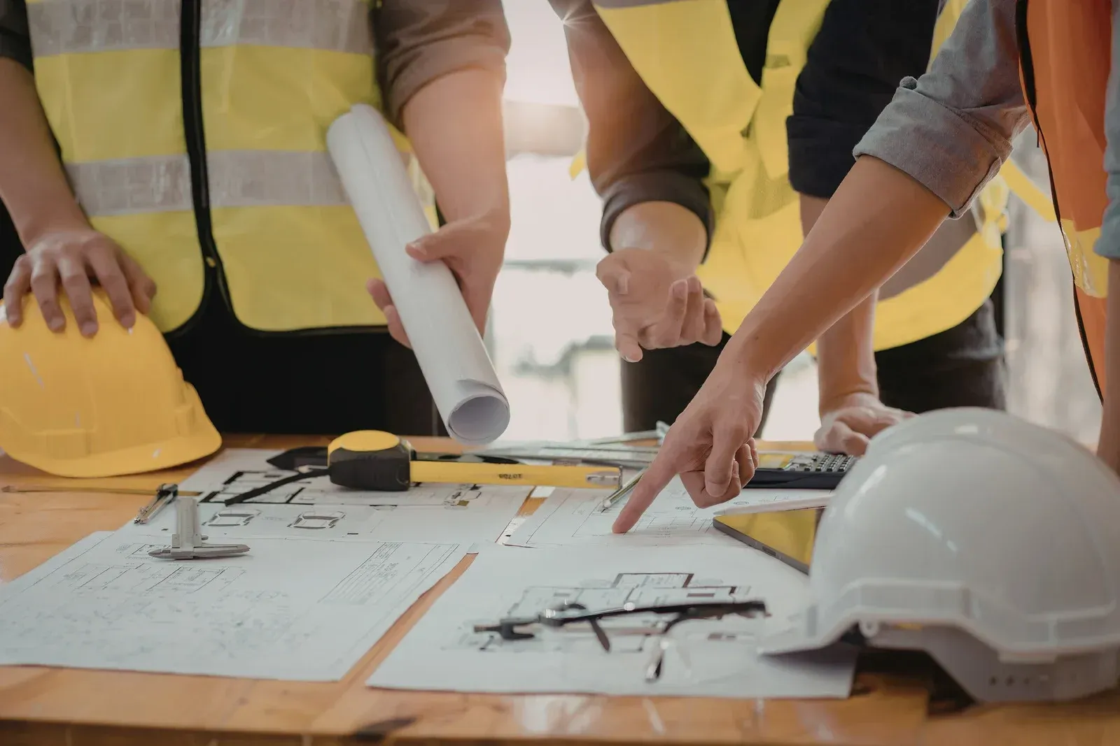 Construction team reviewing blueprints at a worktable with a white hard hat in the foreground