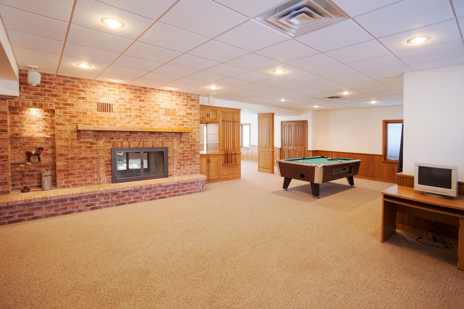 Spacious finished basement with brick fireplace, pool table, carpet, and a small TV on a wooden stand