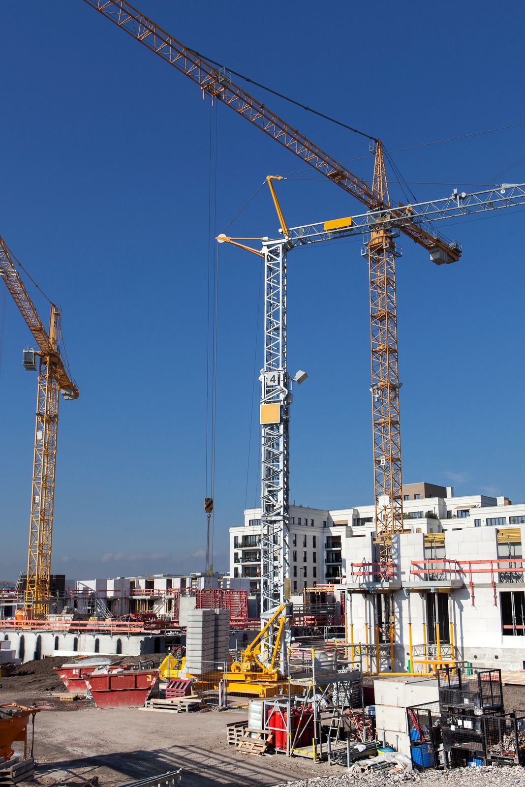 Construction site with tall cranes and a partly built high-rise under a clear blue sky
