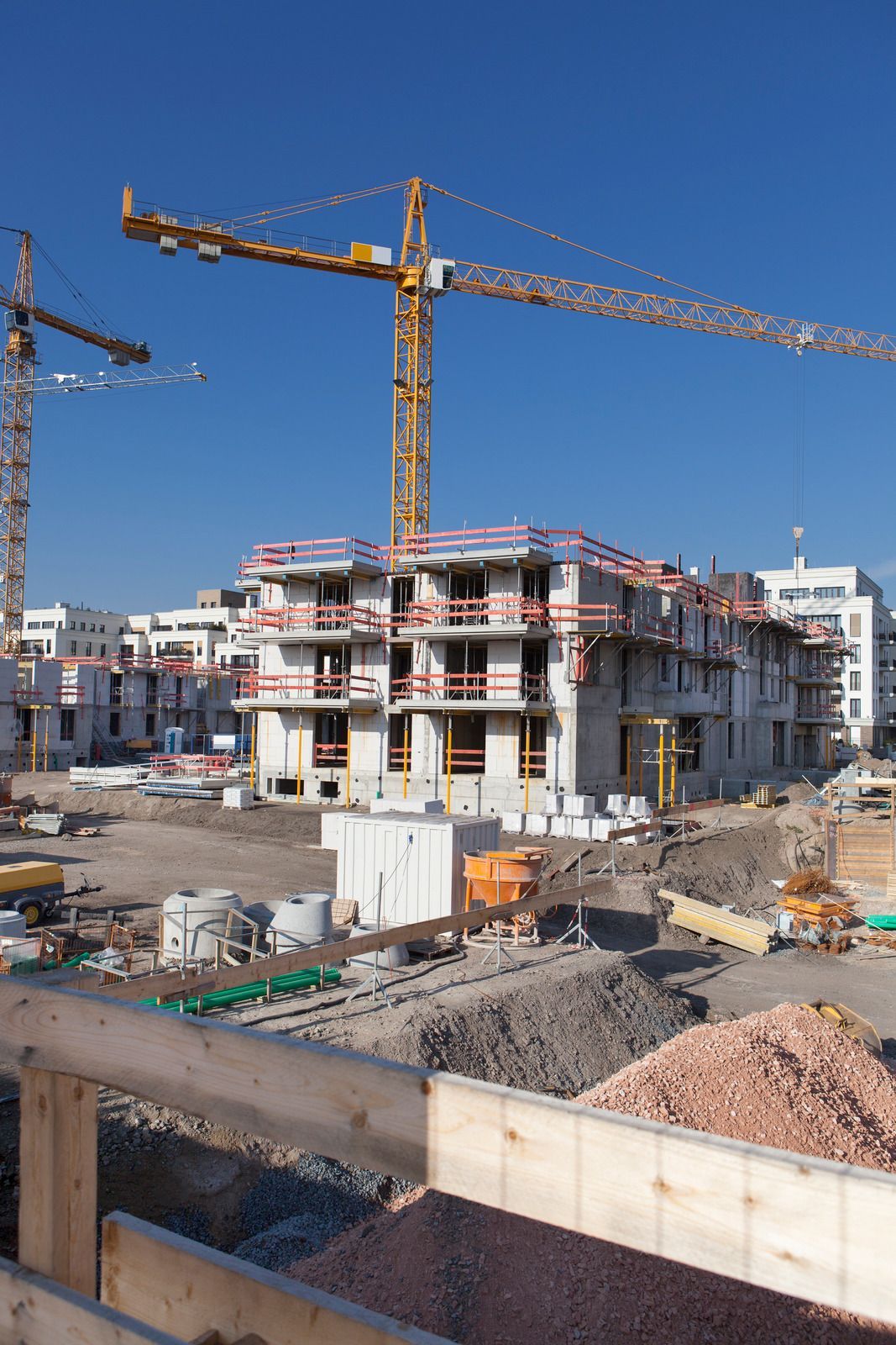 Construction site with a multi-story building and yellow cranes under a clear blue sky