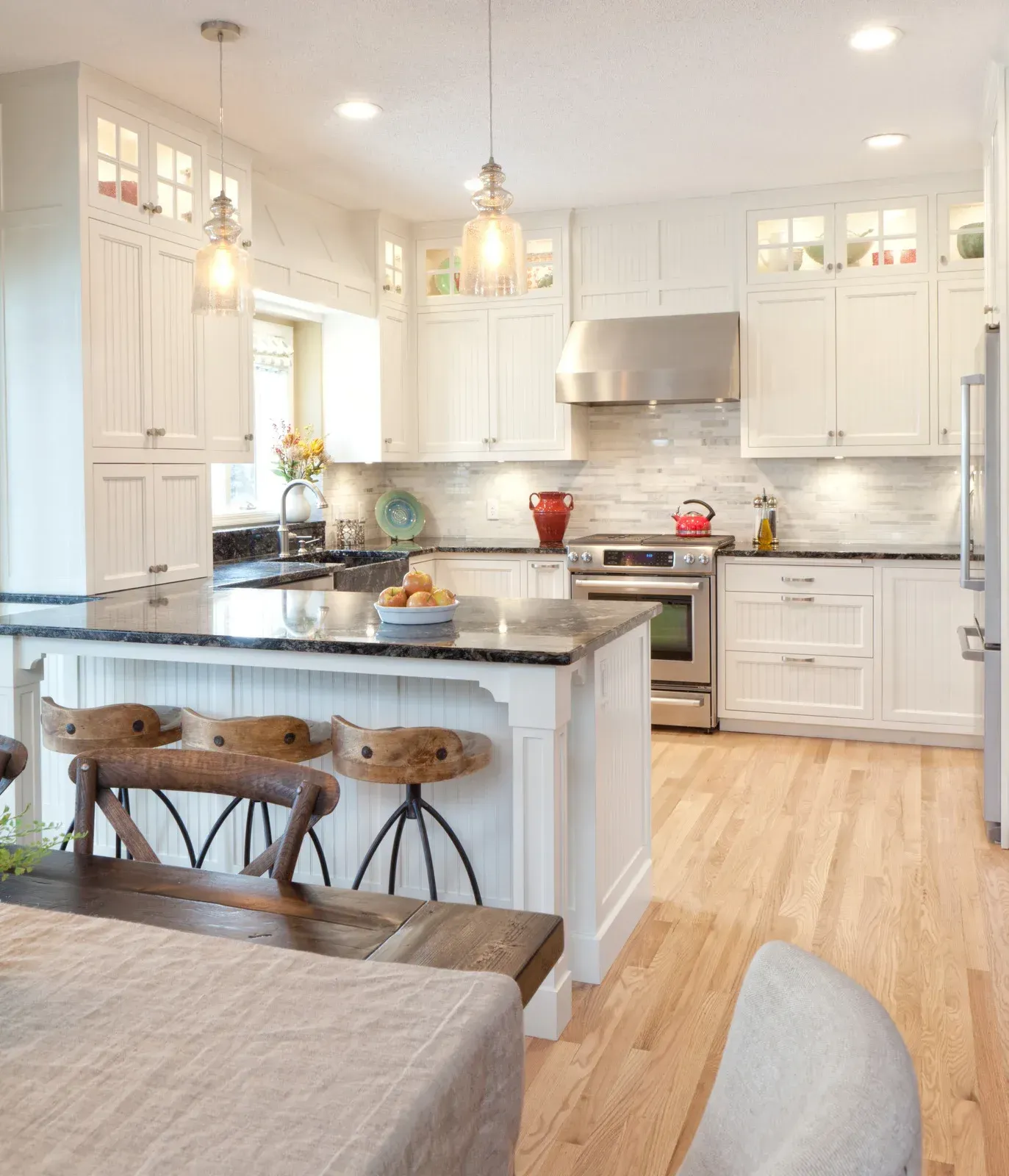 Bright white kitchen with island, pendant lights, stainless appliances, and light wood floors