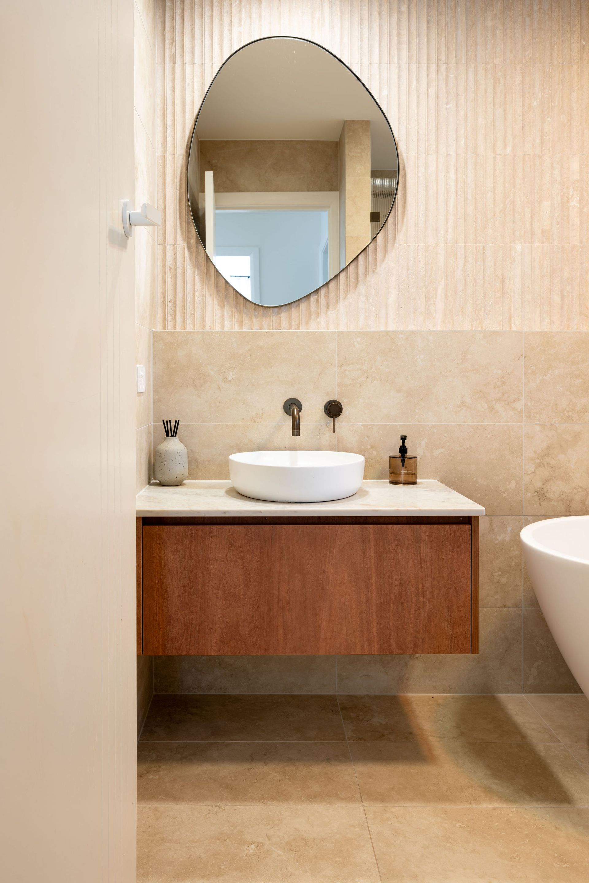 Bathroom with round white mirror, gold fixtures, and tiled wall. — Flow Kitchens in Taree South, NSW