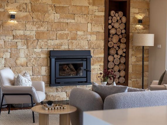 Stone Fireplace With a Black Insert, Flanked by Wall Sconces and a Wood Storage Niche — Flow Kitchens in Taree South, NSW