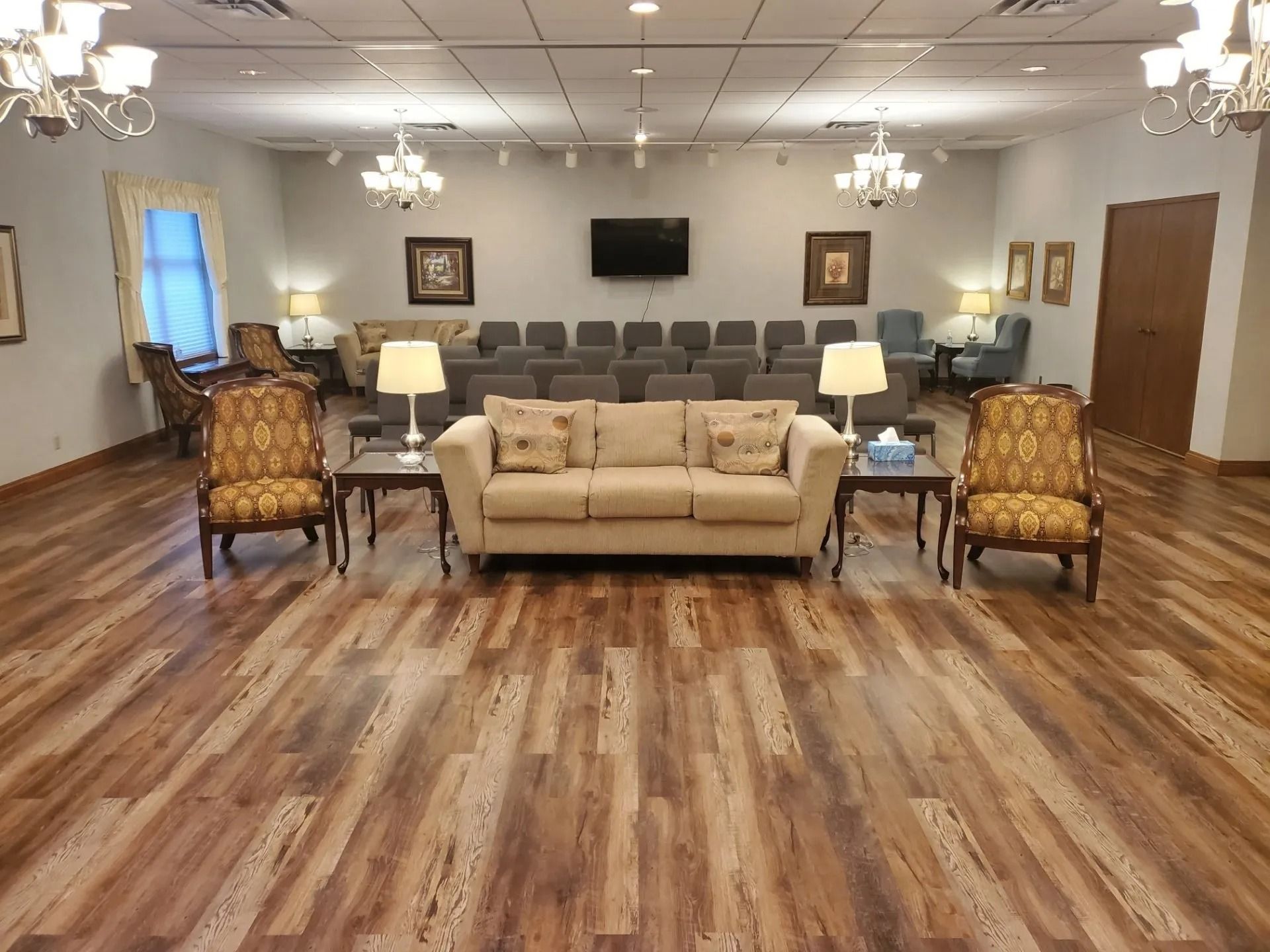 Interior of a formal room with seating, a sofa, chairs, and a small TV on the wall.