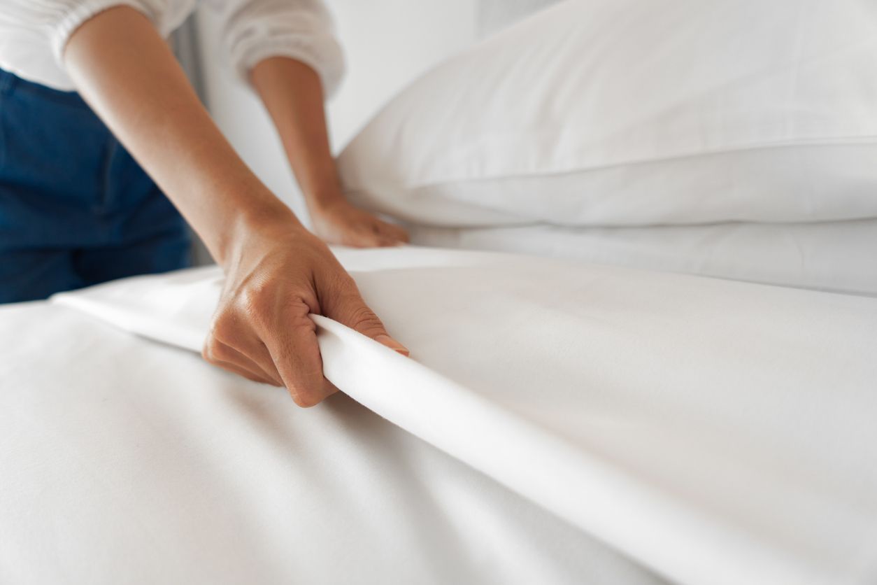 Person making a bed, smoothing white sheets.