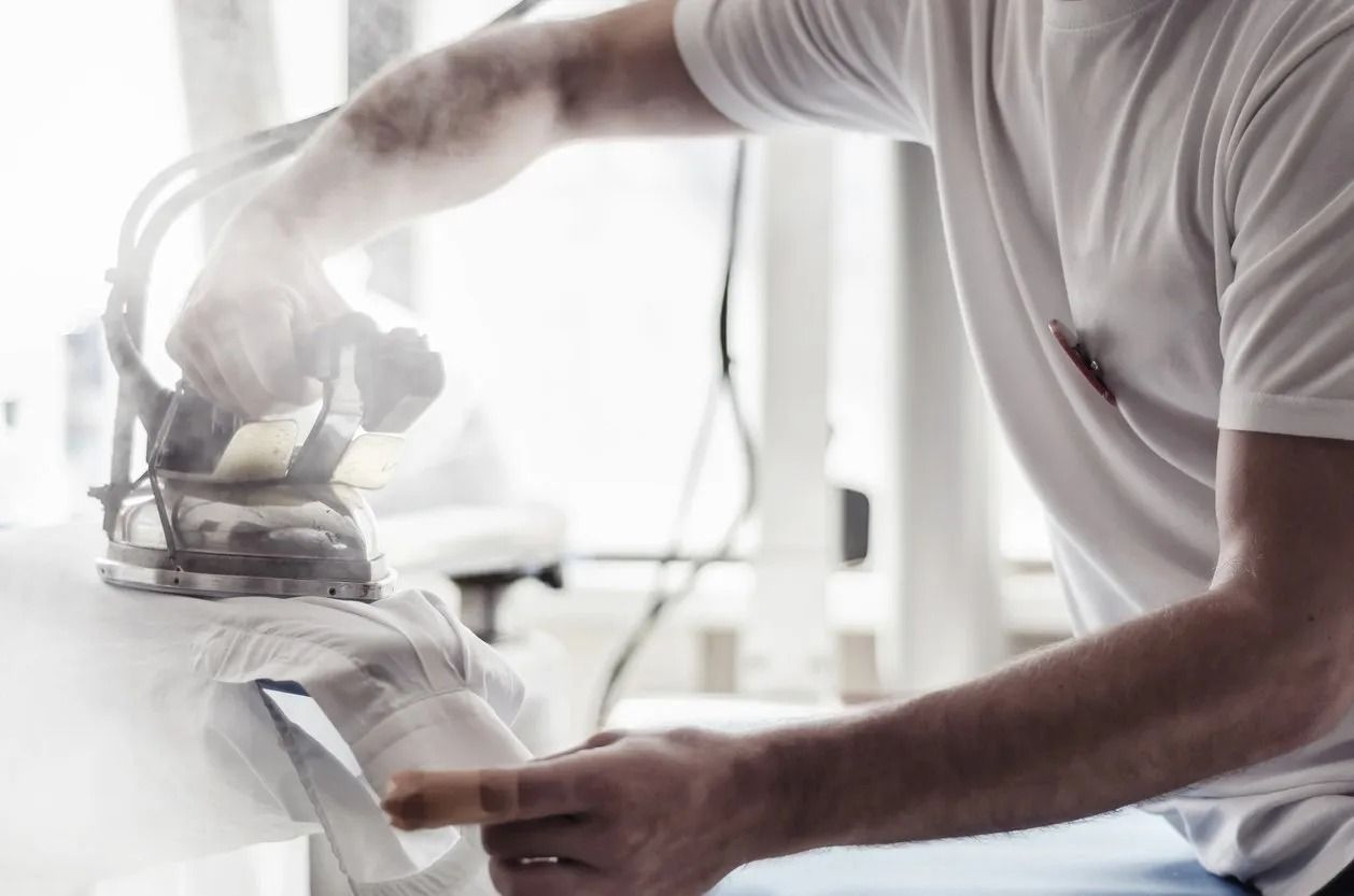 Person ironing a white shirt, steam rising, indoors.