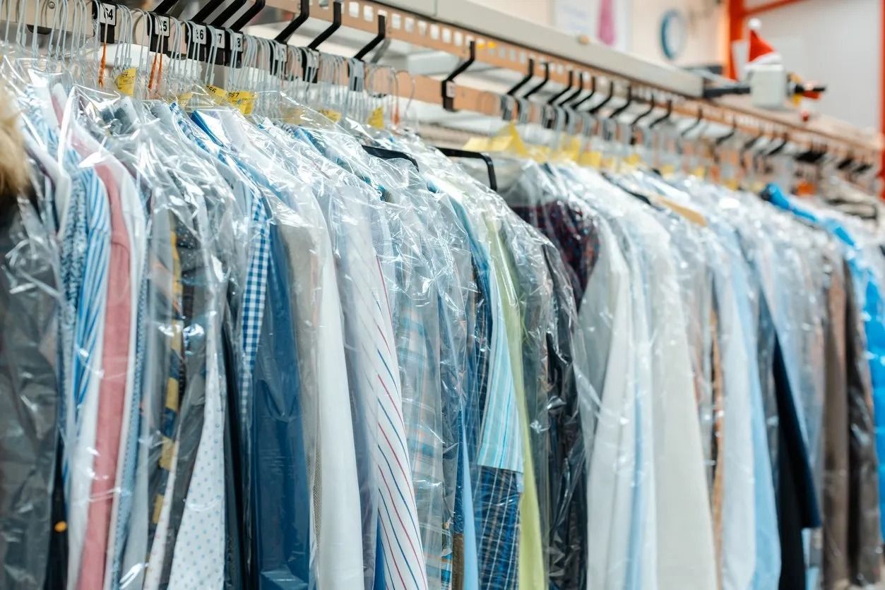 Clothing on hangers, covered in clear plastic, at a dry cleaner.