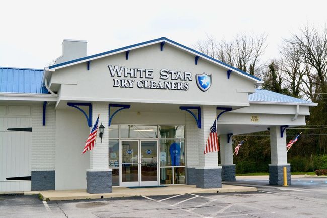 White Star Dry Cleaners storefront with blue and white trim, American flags, and a cloudy sky.