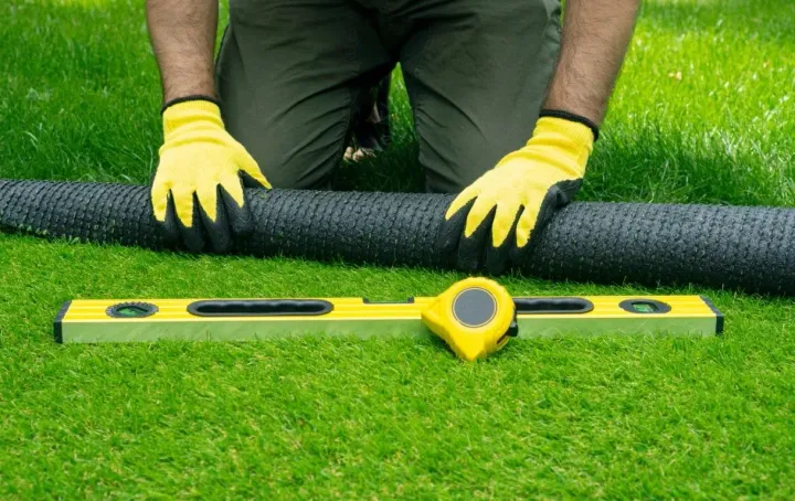 Man using yellow spirit level on green artificial grass turf.
