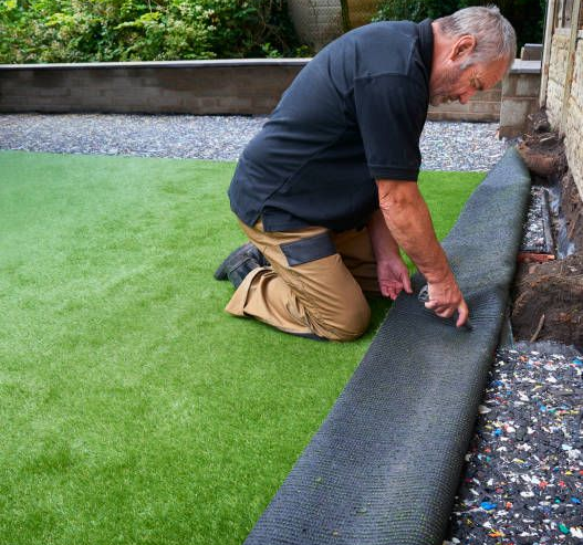 Landscaper cutting artificial turf edge with utility knife.