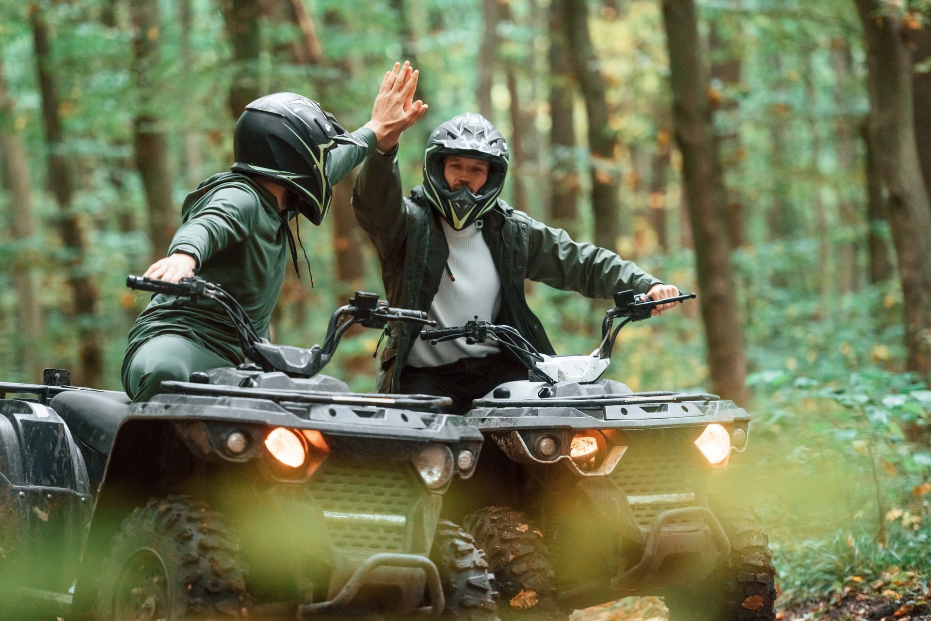 A man and a woman are giving each other a high five while riding an atv in the woods.