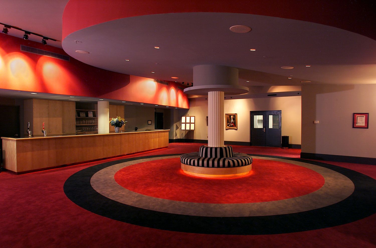 A lobby with red carpet and a striped bench in the middle