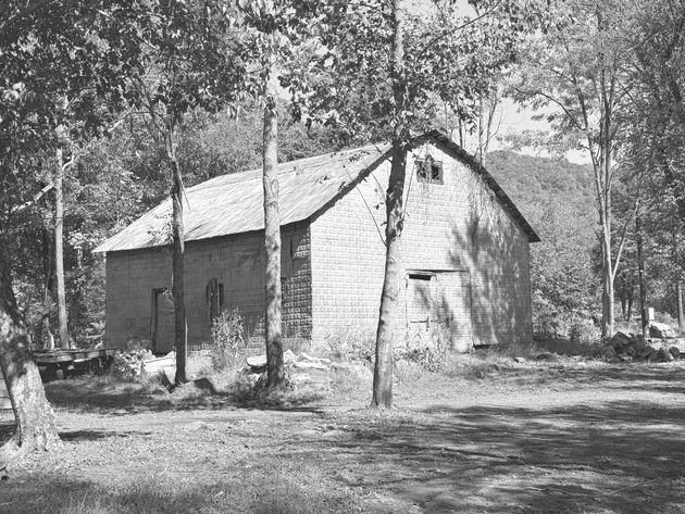 A black and white photo of a barn surrounded by trees.