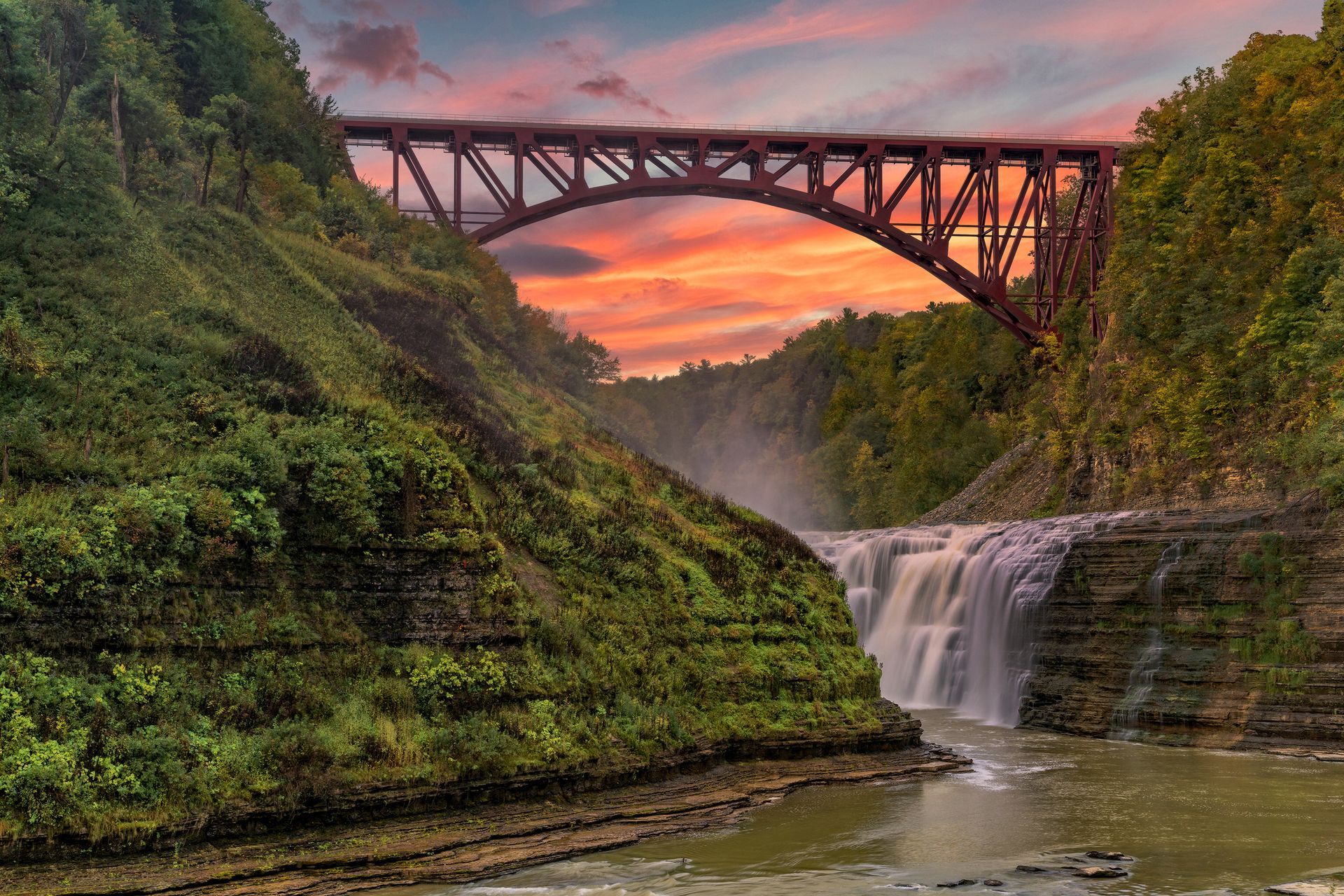 A bridge over a waterfall with a sunset in the background.