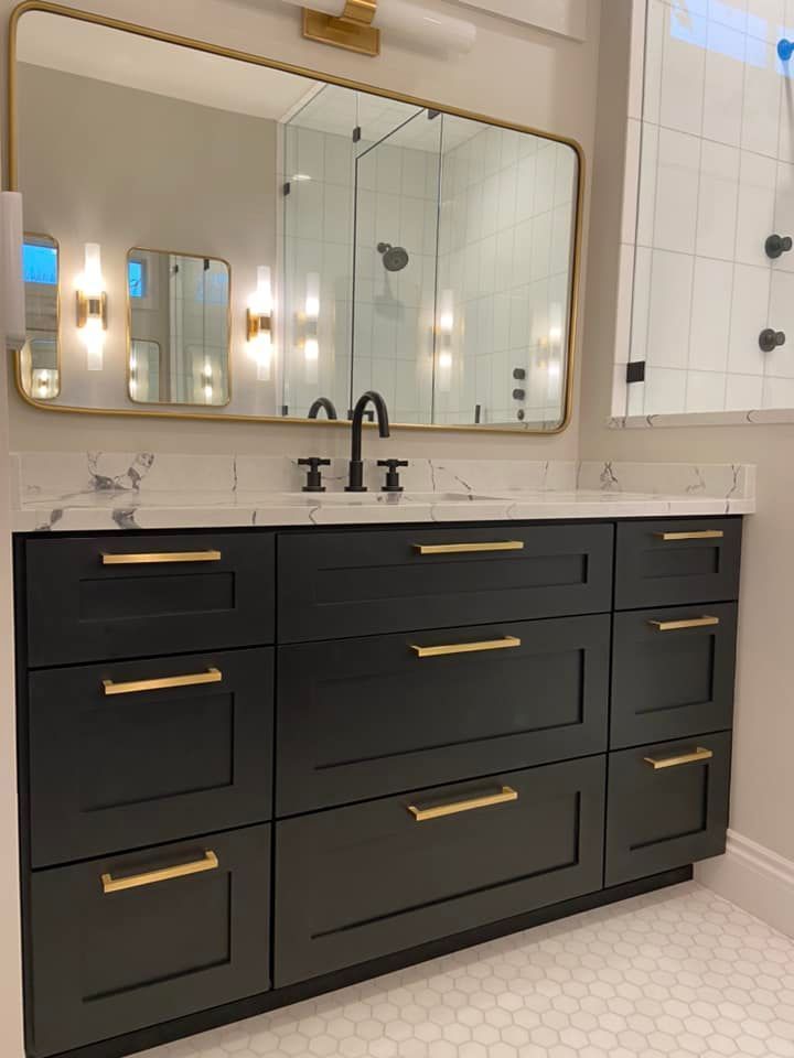 Modern bathroom vanity with black cabinets, brass pulls, white countertop, and large mirror above.