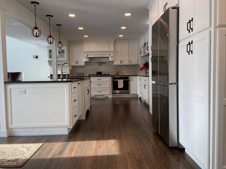 Bright modern kitchen with white cabinets, dark island, stainless appliances, and wood floors