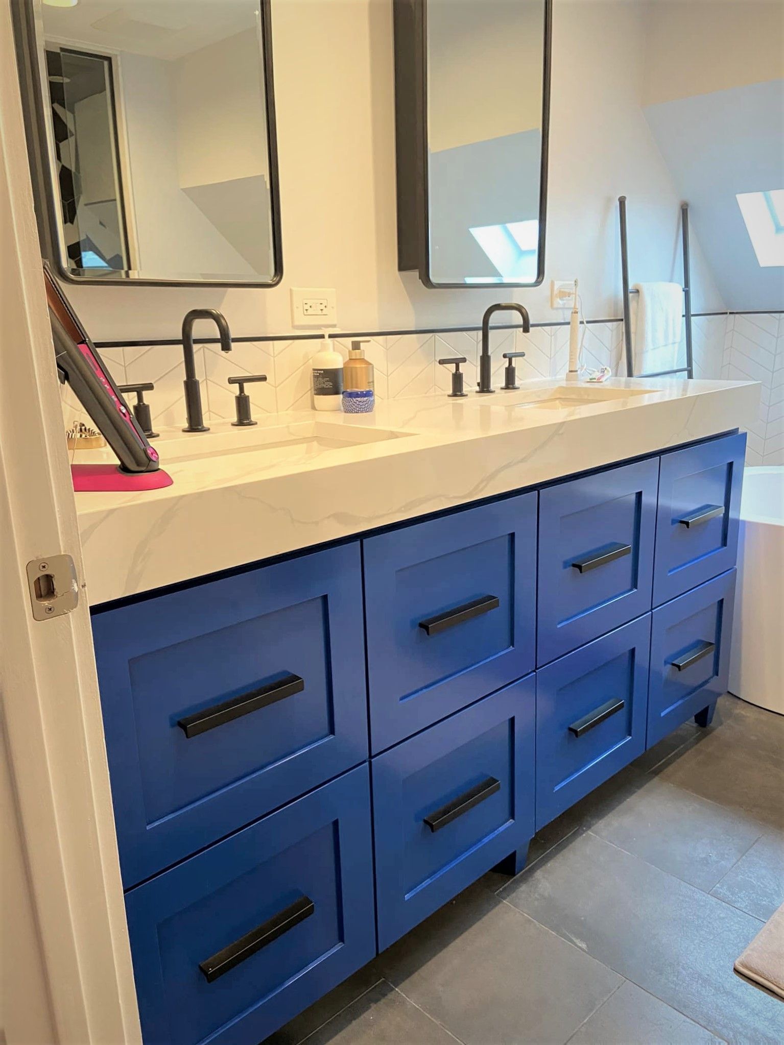 Blue bathroom vanity with double sinks, white countertop, and mirrors above, lit by natural light.