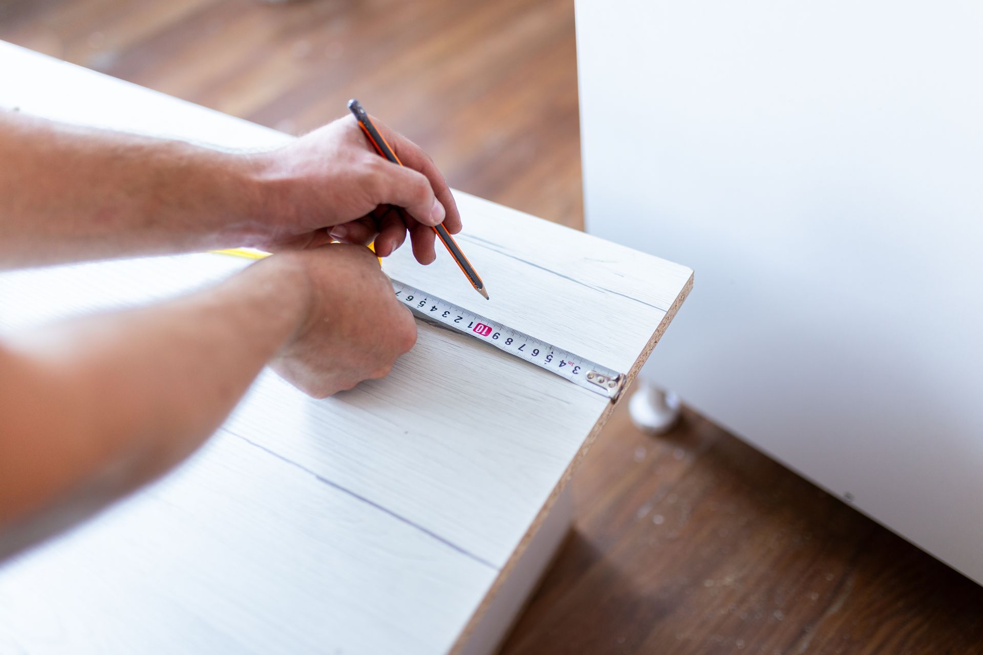Cabinet builder measuring and marking a wood panel before installation