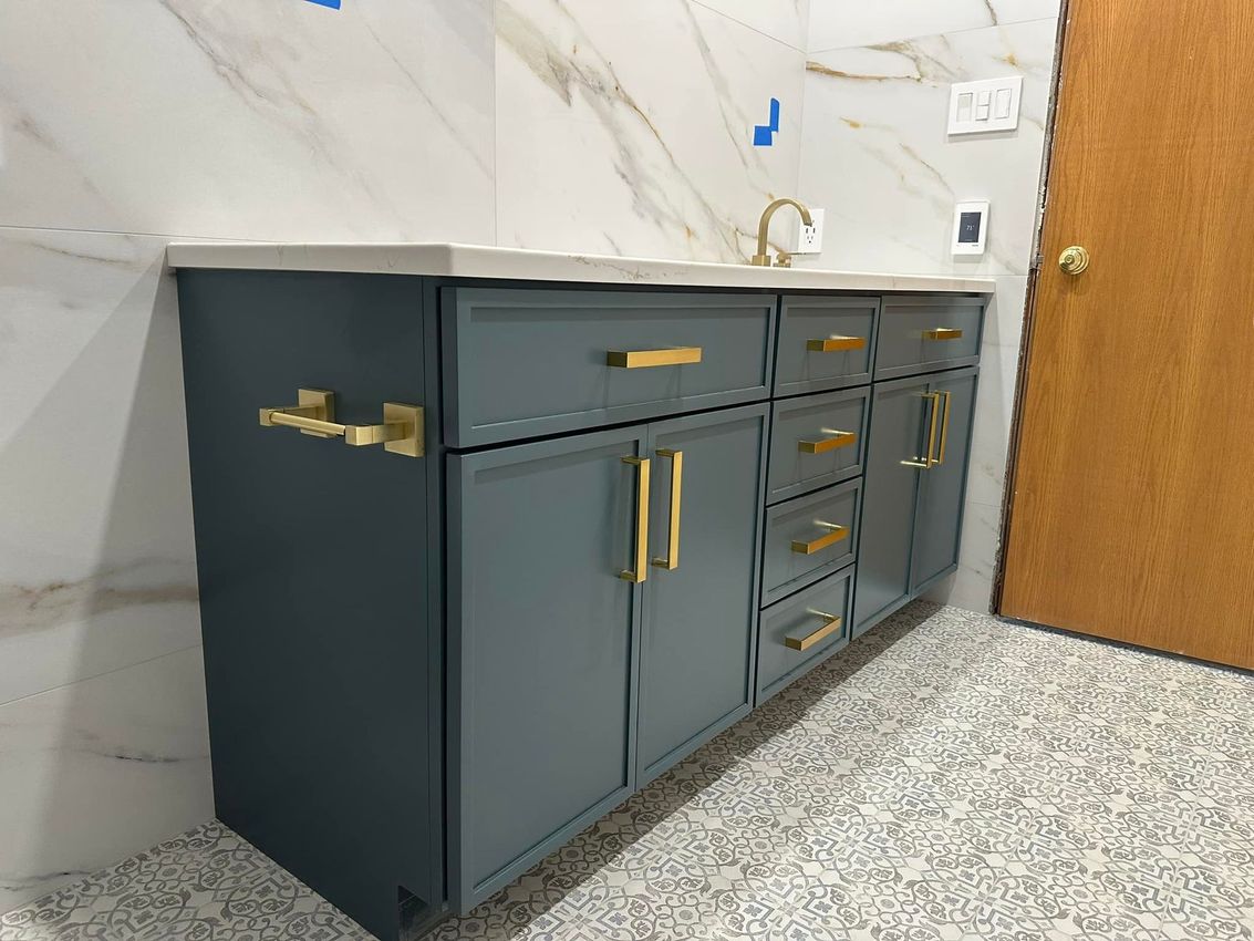 Gray bathroom vanity with gold handles and a marble countertop beside a wooden door