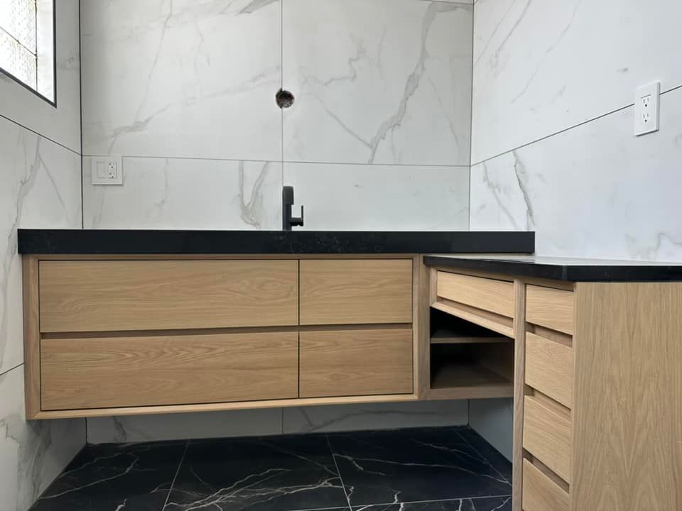 Modern bathroom vanity with light wood cabinets, black countertop, and white marble-look tile walls