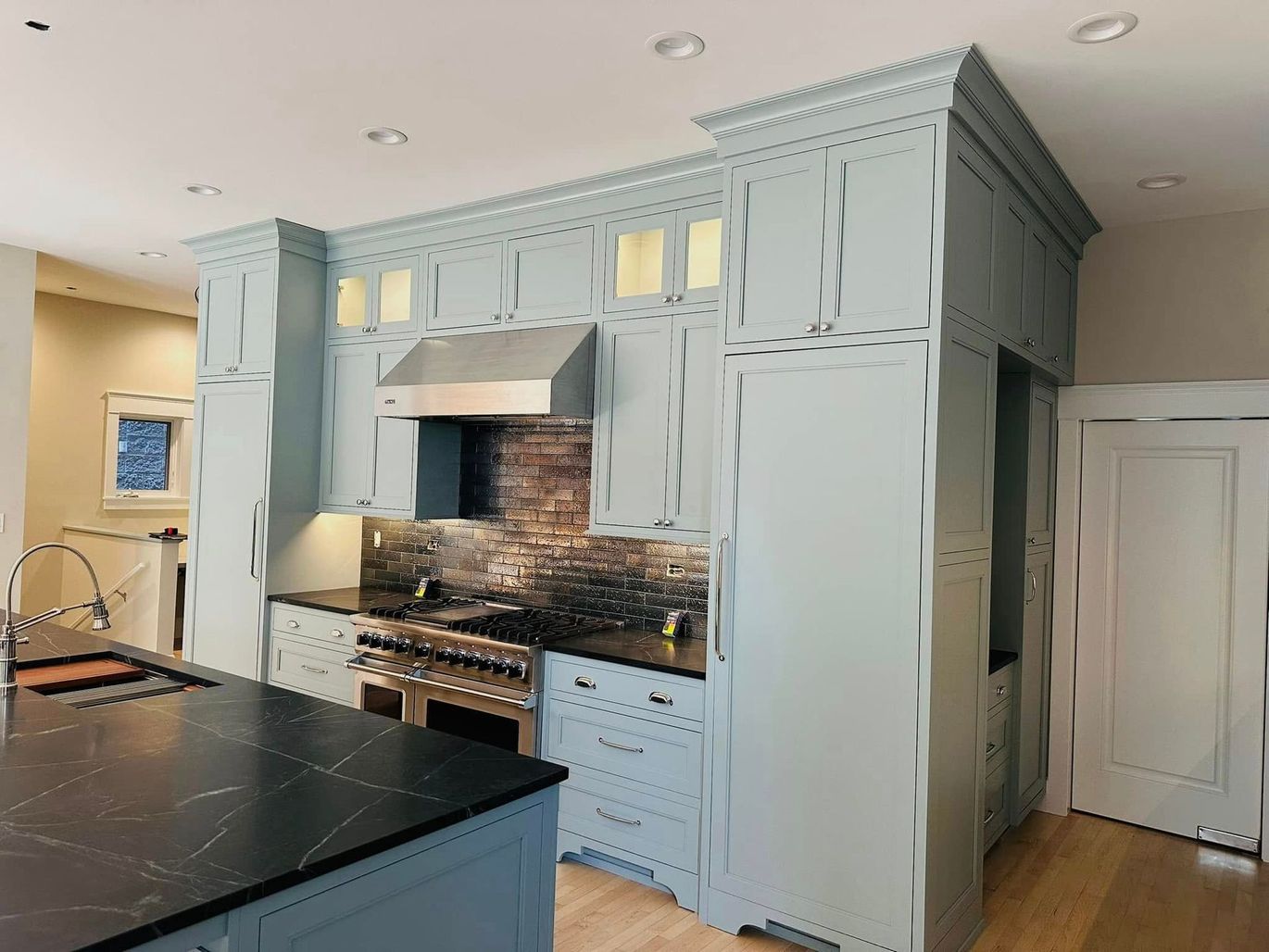 Light blue kitchen cabinets with dark countertop, stainless stove, and central island in a modern kitchen