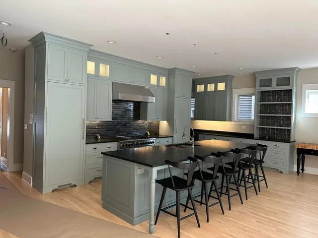 Modern kitchen with gray cabinetry, black island, and four bar stools beside a light wood floor