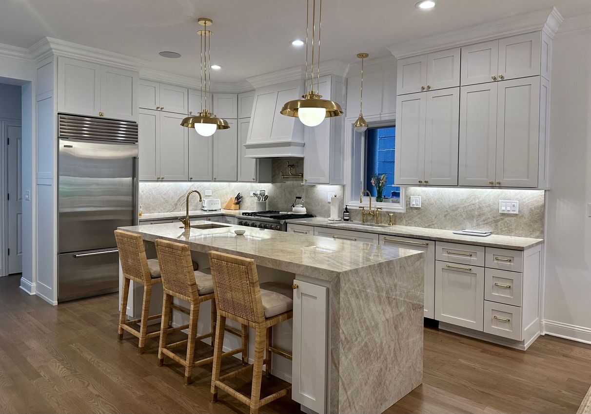 Bright modern kitchen with white cabinets, marble island, wicker stools, and stainless steel refrigerator