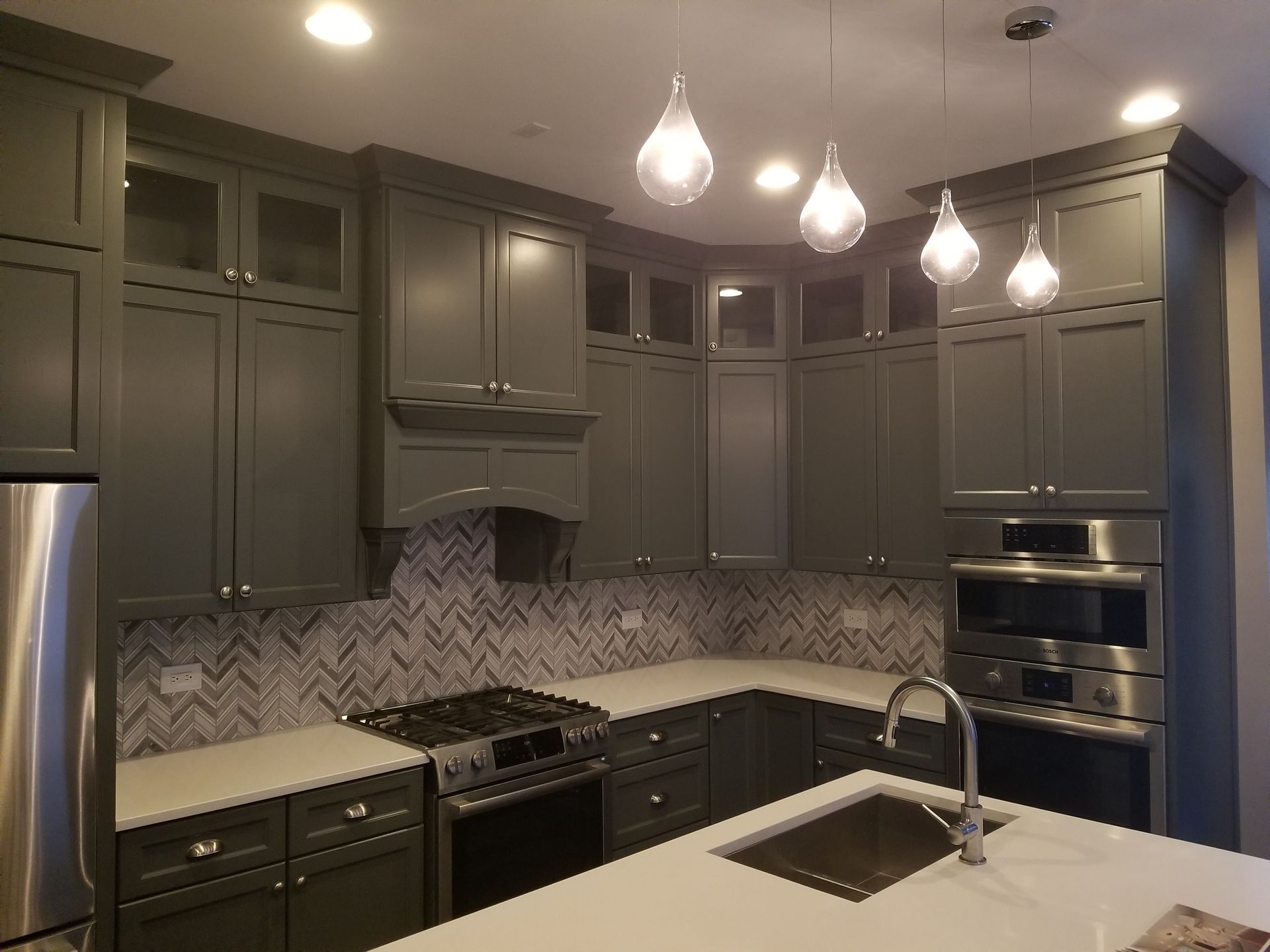 Modern dark-gray kitchen with stainless appliances, pendant lights, and a white island sink