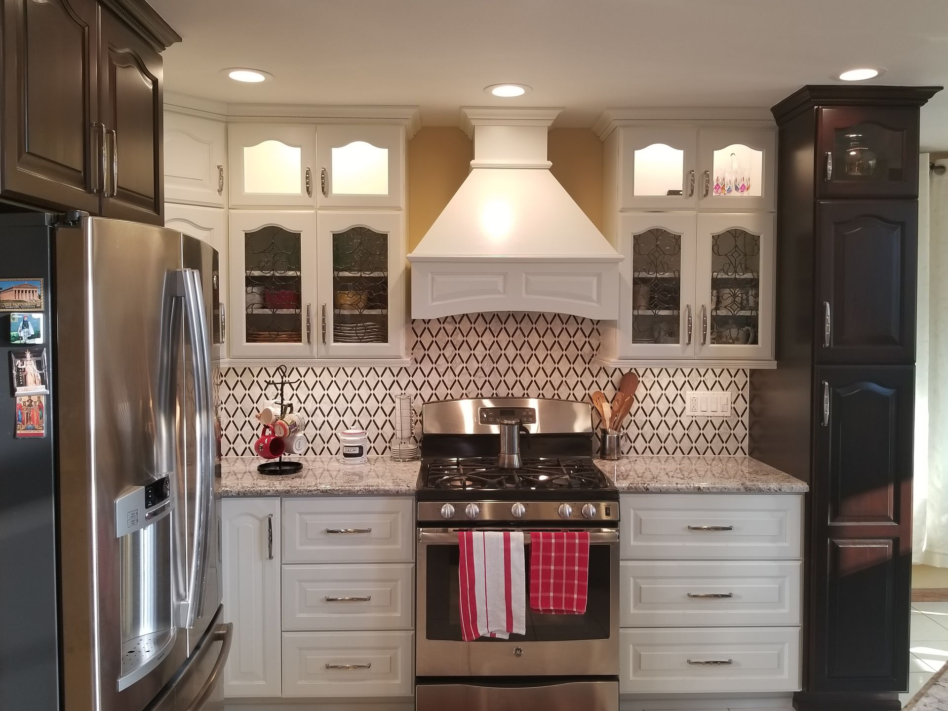 Bright modern kitchen with stainless-steel appliances, white cabinets, mosaic backsplash, and red towels on oven handle