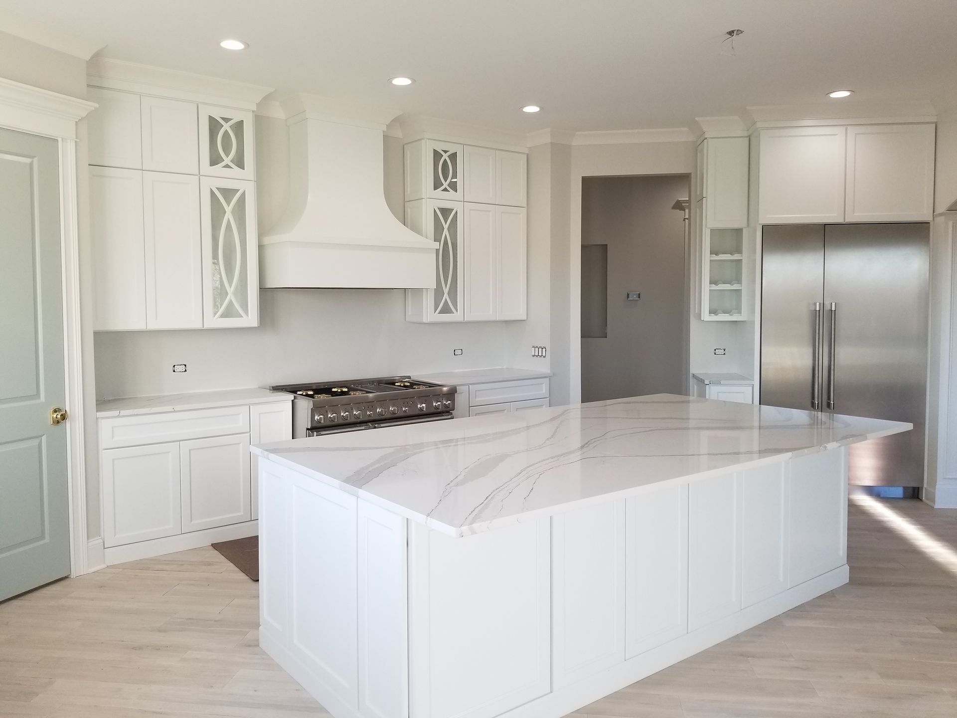 Bright white modern kitchen with large island, stainless fridge, and gas range